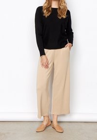 Maglietta nera a maniche lunghe, pantaloni beige a gamba larga e mocassini color sabbia. Tessuti lisci e leggeri. I pantaloni presentano una vita elastica e una vestibilità comoda.