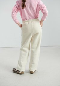 Pantalon en polaire de couleur crème avec une coupe décontractée et une taille élastique. Associé à des chaussures marron et à motifs. Chemise rose à manches longues visible.