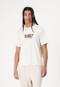 Cremefarvet bomulds t-shirt med et dristigt sort og rødt grafisk design, der står "LOS ANGELES California", og en afslappet pasform med korte ærmer.