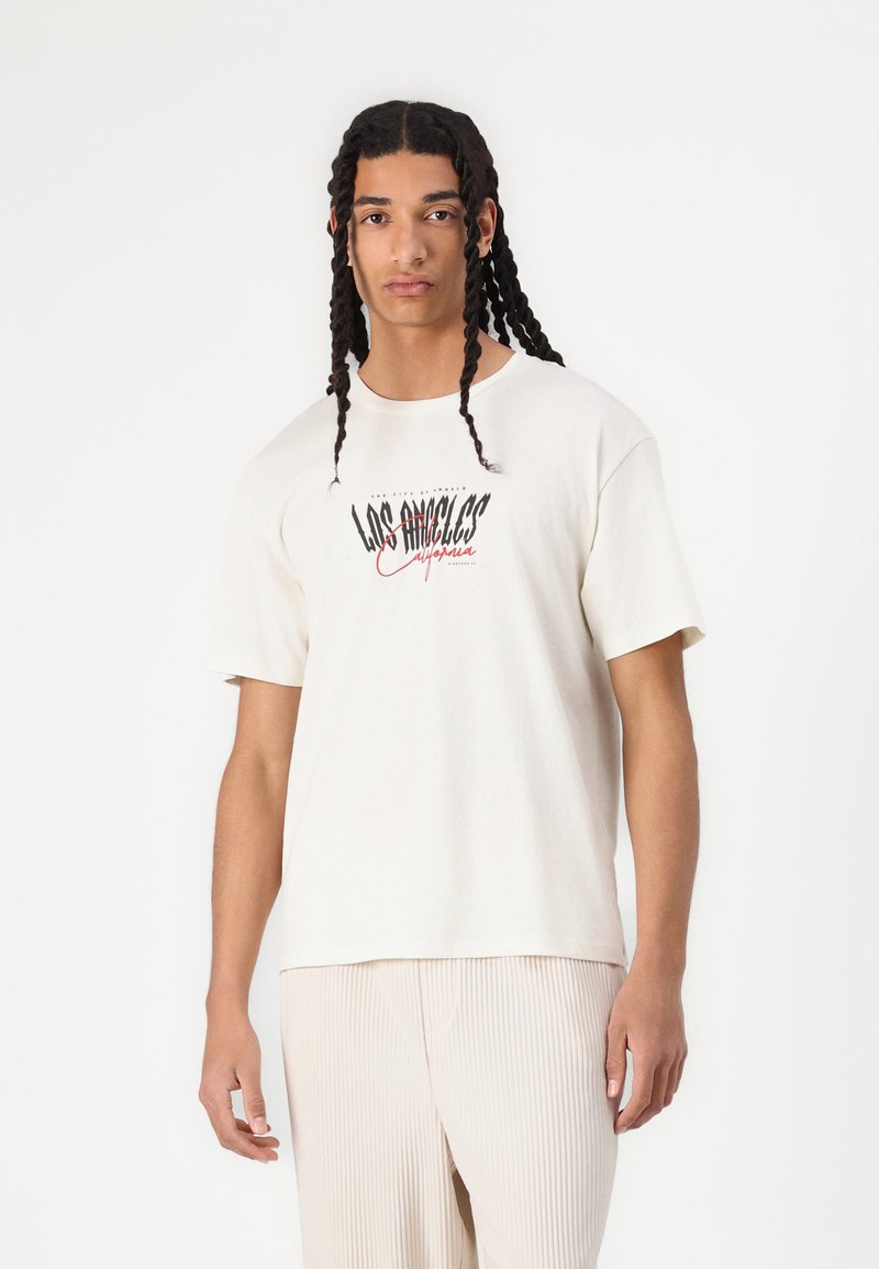 Cremefarvet bomulds t-shirt med et dristigt sort og rødt grafisk design, der står "LOS ANGELES California", og en afslappet pasform med korte ærmer.