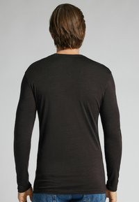 Langärmliges schwarzes Hemd aus einem glatten, leichten Stoff. Taillierte Passform mit rundem Ausschnitt und einfachem Nähdetail am Saum.