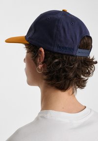 Navy blue cotton cap with an orange visor and adjustable strap. Features embossed "hummel" logo on the back near the strap.