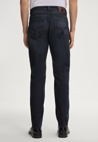Jean en denim bleu foncé vu de l'arrière, avec deux poches arrière, une étiquette en cuir au niveau de la taille, et une coupe droite.