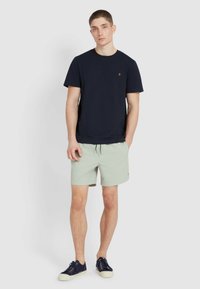 T-shirt crewneck blu navy, pantaloni corti verde chiaro e sneakers blu navy. La t-shirt presenta un piccolo logo; i pantaloni corti hanno cordoncino e tasche laterali.