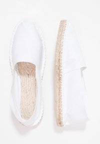 Espadrillas bianche in tela con forma piatta, suola in giute e bordo cucito. Presentano un lato aperto per traspirabilità e comfort.