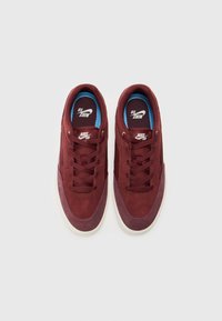 Bordeaux ruskinn sneakers med en marineblå innside, med en hvit gummisåle og flate lisser. Nike SB-logo på tungen og siden.