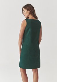 Sleeveless green dress made of smooth fabric, featuring a simple, straight silhouette with a rounded neckline and knee-length design.