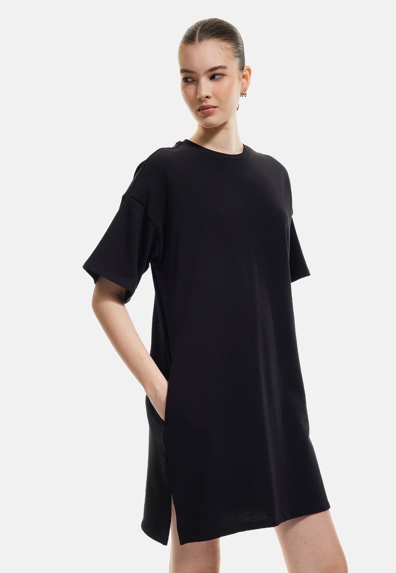 Musta lyhythihainen mekko, joka on valmistettu pehmeästä kankaasta. Mekossa on rento istuvuus, sivutaskut ja hieman pidennetty helma, jossa on sivuaukot.