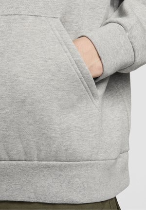 Main partiellement dans la poche avant d’un sweat gris clair avec poignets et ourlet côtelés.