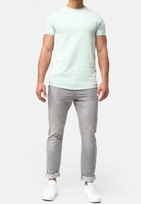 Valkoinen mintunvihreä puuvillapaita lyhythihaisilla hihoilla, yhdistettynä rullattuihin vaaleanharmaisiin farkkuihin ja valkoisiin tennareihin. Yksinkertainen, koristamaton muotoilu.