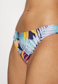 Bikiniunderdel med flerfärgad tropisk lövmönster. Funktioner med låg midja och elastisk midjeband. Mjuk tygtextur.