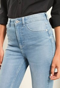 Fénykék farmernadrág, slim fit fazonban, elülső zsebbel, cipzáros és gombos záródással, valamint diszkrét varrási részletekkel.