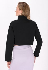 Sweatshirt negru scurt cu guler înalt, mâneci lungi și o textură netedă. Asortat cu o fustă mov cu țessătură în relief, având un design mulat.