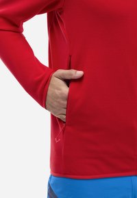 Chemise à manches longues texturée rouge avec une poche zippée sur le côté, design ajusté et bord contrastant à l'ourlet.