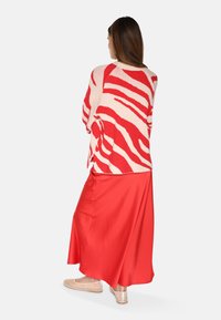Gebreide trui met een rood en crèmekleurig zebra-strepenpatroon, gecombineerd met een lange rode satijnen rok en beige instappers.