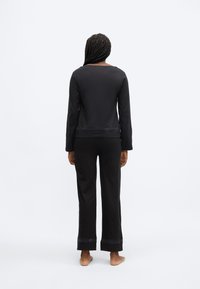 Črni komplet za sprostitev, ki vključuje dolg rokav in lahke hlače, izdelan iz mehke tkanine z gladko teksturo in subtilnimi detajli na robovih.