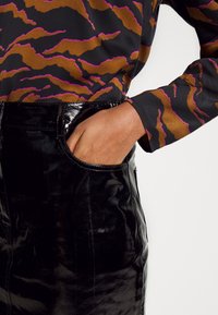 Pantalons en cuir verni noir avec une texture lisse et un grand éclat, associés à un haut à manches longues avec un motif ondulé brun et rose.