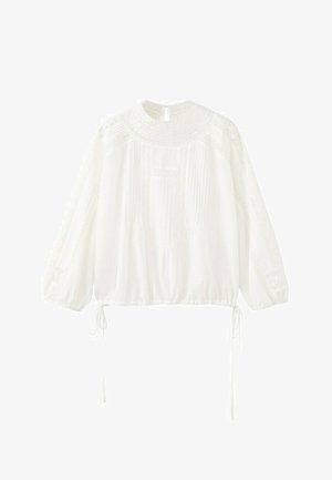 Hvid bluse med lange ærmer, blonder på bærestykke og ærmer, pressede folder foran, elastisk kant med bånd i siderne og nøglehulslukning med knap i nakken.