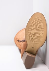 Zapato de ante marrón exhibido de forma horizontal, con enfoque en la suela que presenta un patrón texturizado y la talla marcada como 37.