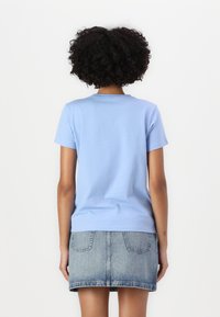 Tricou din bumbac de culoare albastră deschisă, cu mâneci scurte, decolteu rotund și o croială lejeră, asortat cu o fustă din denim cu talie înaltă și buzunare.