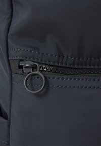 Tessuto blu navy con una consistenza liscia, dotato di una tasca con zip e un il tirante nero, con cuciture blu a contrasto lungo i bordi.