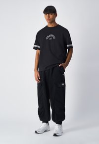 Zwarte korte mouwen T-shirt met grijzen "Champion" logo, gecombineerd met losse zwarte cargobroek met zijzakken en elastische boorden bij de enkels. Witte sneakers.