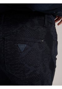 Jeans in denim blu scuro con un motivo testurizzato, dotati di un'etichetta a forma di triangolo sulla tasca posteriore e dettagli di cucitura standard.