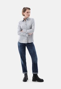 Gray linen button-up shirt with floral embroidery, paired with dark blue rolled-cuff denim jeans and black chunky ankle boots.