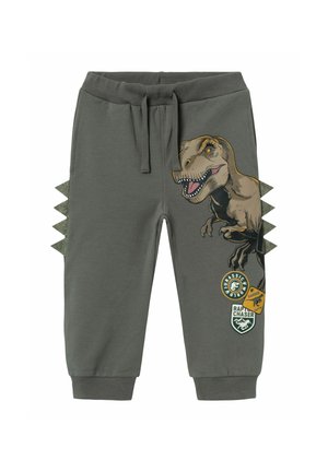 Pantaloni della tuta grigi in cotone, dotati di una grafica di un dinosauro, dettagli in tessuto verde che ricordano le spine e diverse toppe stampate.
