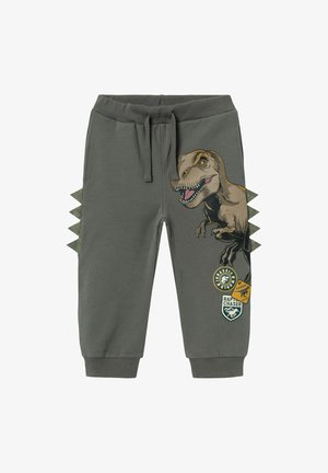 Pantaloni della tuta grigi in cotone, dotati di una grafica di un dinosauro, dettagli in tessuto verde che ricordano le spine e diverse toppe stampate.