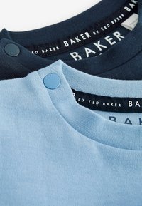 Zwei T-Shirts mit Rundhalsausschnitten. Eines ist hellblau, das andere dunkelblau. Beide haben kontrastierende Stoffstrukturen und Druckknopfdetails.