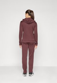 Maroon activewear set featuring a hooded sweatshirt and matching pants. Smooth fabric, long sleeves, and fitted cuffs provide comfort.