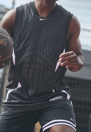 Koszykarz w czarnym stroju Nike i spodenkach kozłuje piłkę Spalding na zewnętrznym boisku.