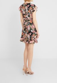 Robe florale noire avec de courtes manches à volants, taille cintrée, longueur cheville, et ourlet volanté. Associée à des sandales à talons hauts nude claires.
