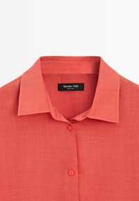 Chemise corail à manches longues avec col, deux boutons visibles et une étiquette noire Massimo Dutti à l'intérieur de l'encolure.
