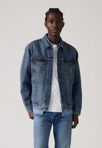 Chaqueta de denim en un lavado medio con un corte clásico, que cuenta con dos bolsillos en el pecho, cierre de botones y un ligero desgaste en las mangas.
