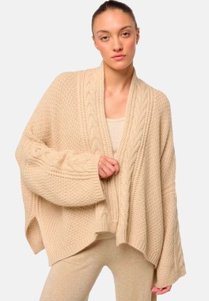 Beige gestrickte Strickjacke mit einem strukturierten Muster, weiten Ärmeln und einem Schalkragen. Mit Kabelstrickdetails entlang der vorderen Kanten.