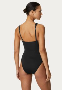 Maillot de bain noir avec des bretelles ajustables, un design à jambe haute et une texture sans couture, offrant une silhouette épurée et ajustée.