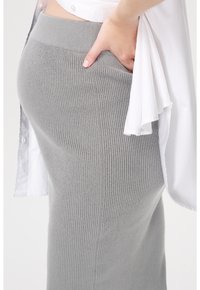 Grijze geribbelde gebreide rok met een hoge tailleband en rekbaar materiaal. Een wit shirt is eroverheen gedragen, waardoor de rok gedeeltelijk bedekt is.