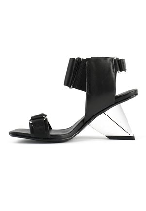Sandale noire en cuir avec une large sangle à la cheville, dotée d'un talon conique géométrique en argent et d'une sangle plate sur les orteils.