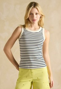 Prúžkovaná tielko v krémovej a námorníckej modrej farbe, s okrúhlym výstrihom a bezrukávovým dizajnom. Skombinujte s žltými šortkami ozdobenými malými detailmi.