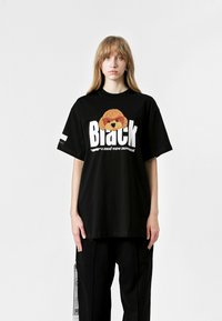 Camiseta negra de gran tamaño con un gráfico texturizado de un perro y texto grande en blanco. Manga corta y escote redondo; combinada con pantalones negros.