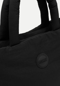 Melna iepirkumu soma ar mīkstu struktūru un izturīgām rokturiem. Vienā pusē ir apļveida, izcelts Colmar logo. Gluda auduma virsma.