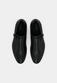 Μαύρα δερμάτινα παπούτσια με λεία επιφάνεια, αμυγδαλωτό σχήμα μύτης και λεπτομέρεια με αγκράφα στο πλάι. Μινιμαλιστικός σχεδιασμός χωρίς ορατά σχέδια.