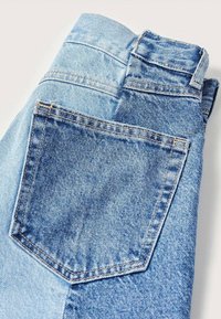 Jean en denim bleu bicolore plié avec une poche arrière visible et une passants de ceinture sur un fond clair.