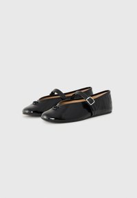 Black patent leather ballet flats with a round toe, a single adjustable strap, and a decorative bow detail on the front.