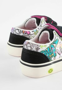 Sort ruskind og mønstrede kanvas sneakers med en hvid sål, der har farverige graffitidesigns og et grønt smiley ansigt som detalje.