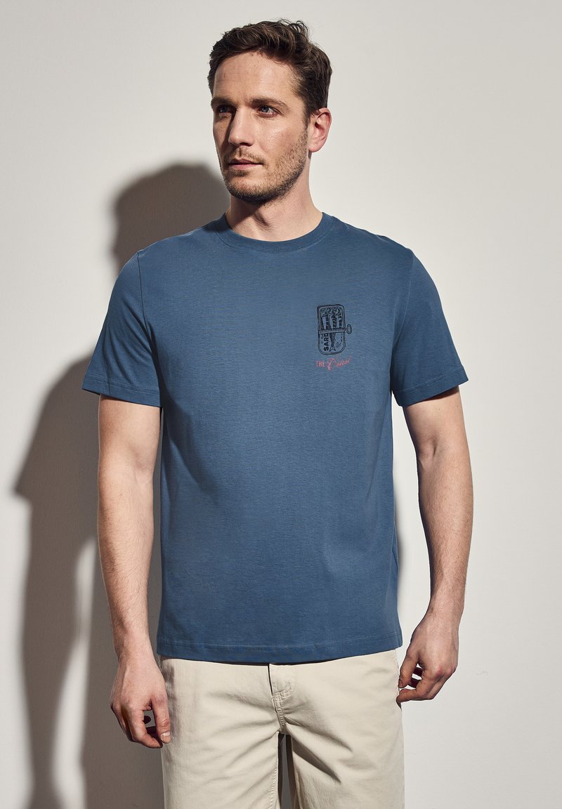 Modrá bavlněná tričko s krátkým rukávem, s grafickým potiskem na levé části hrudníku. Design obsahuje text a geometrický vzor.
