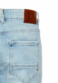 Jasnoniebieskie dżinsy z denimu z brązową skórzaną naszywką na pasku i jedną tylną kieszenią z podwójnym szyciem.