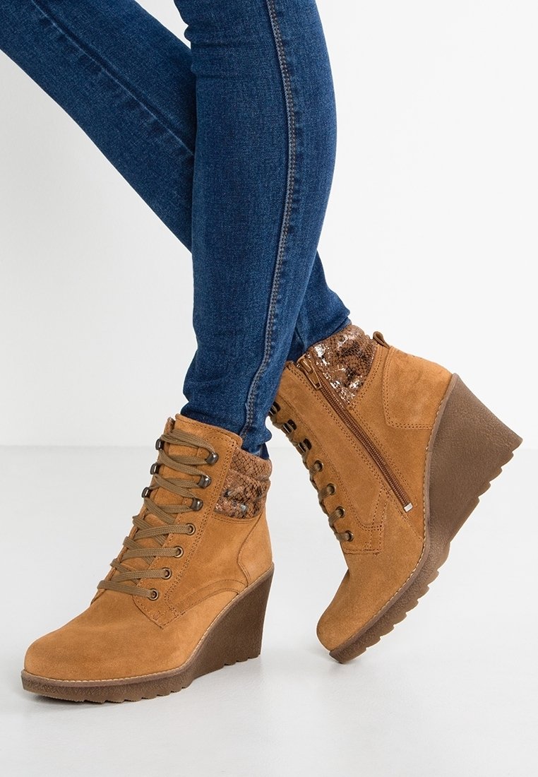 Jambes en jean skinny bleu portant des bottines compensées marron clair avec lacets à l'avant, fermeture éclair latérale et détail texturé au col.